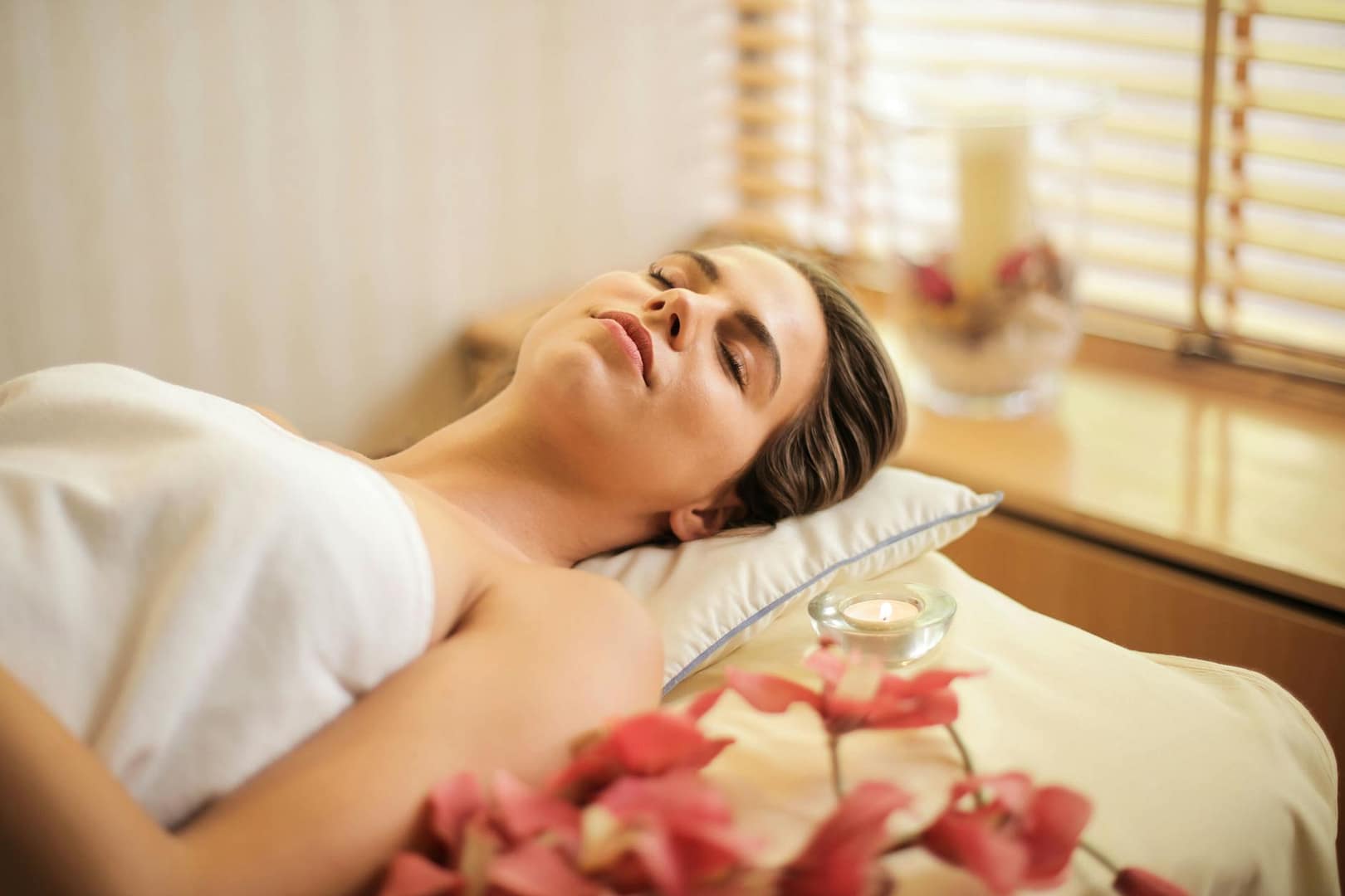 woman in wrapped in white towel lying on ayurvedic massage bed with eyes closed